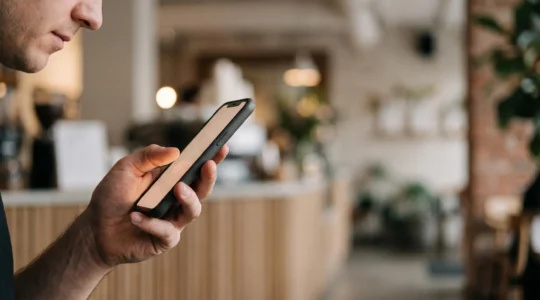 Une main tenant un smartphone dont l'écran diffuse une lumière chaleureuse, symbolisant la connexion et la fidélité entre une marque et son client